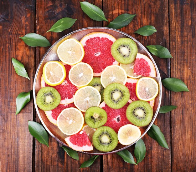 Ripe slices lemon kiwi and grapefruit on tray on wooden background