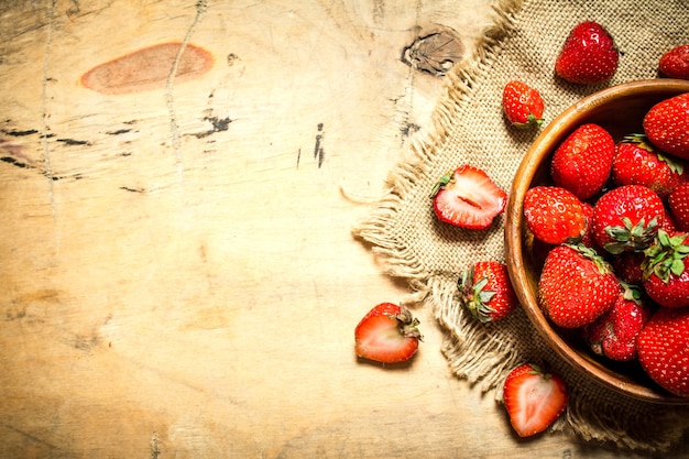 Ripe strawberries in bowl on sack on wooden table.