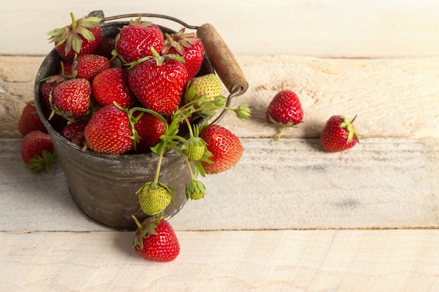 Ripe strawberries in a bucket on a wooden surface