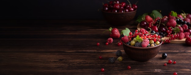 Ripe strawberries, cherries, currants, raspberries, gooseberries in a bowl on a dark wooden background, summer berries, banner, rustic style.