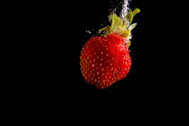 Ripe strawberries fall into the water raising splashes and air bubbles