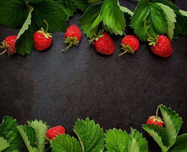 Foto fragole e foglie mature su sfondo nero. vista dall'alto