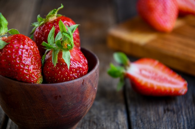 Ripe strawberries lie in a wooden dish in the kitchen on a wooden table