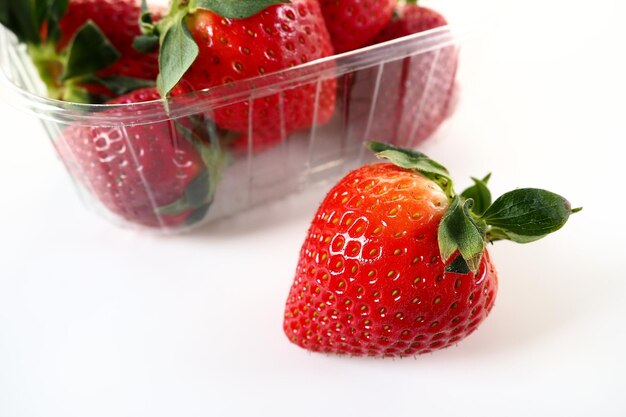 흰색 배경에 플라스틱 패키지에 익은 딸기 고객에게 판매하기 위해 컨테이너에 있는 맛있는 신선한 딸기 식품을 신선하게 유지 건강한 식품 용기에서 딸기 한 개를 꺼냈습니다