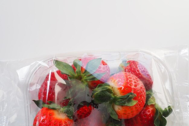 Foto fragole mature in una confezione di plastica su sfondo bianco deliziose bacche fresche in un contenitore per la vendita ai clienti mantenimento del cibo fresco vitamine e microelementi per alimenti sani