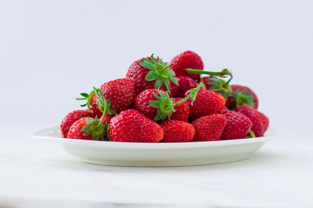 Спелая клубника на тарелке на белом фоне Летние ягоды