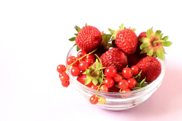 Ripe strawberries and red currants in a glass cup on a white background side view space for text