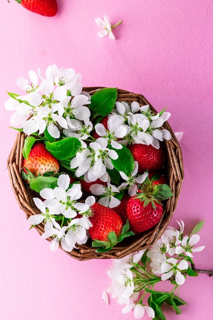 Ripe strawberries and white flowers lie in a wicker basket on a pink background