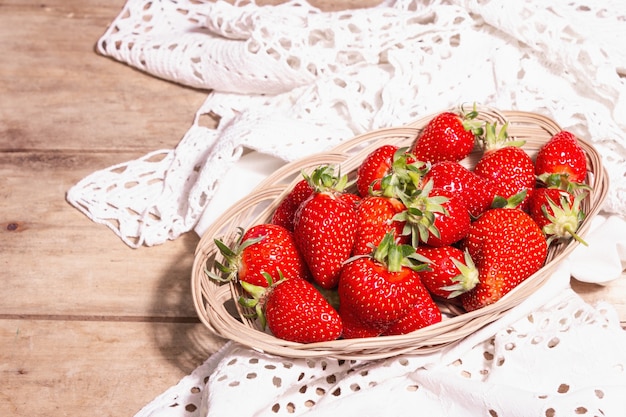 Ripe strawberries in wicker plate. Fresh berries, aromatic mint. Old wooden table, vintage crocheted napkin, rustic style, copy space