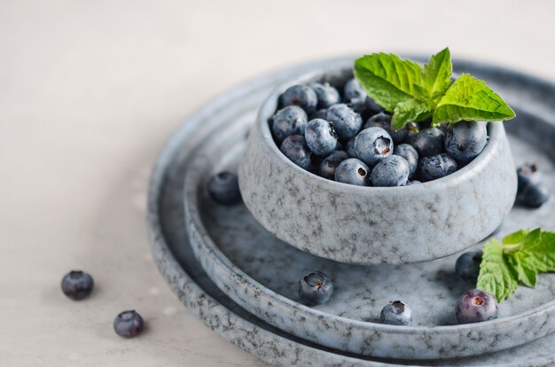 Ripe sweet blueberries in blue bowl on a gray concrete.