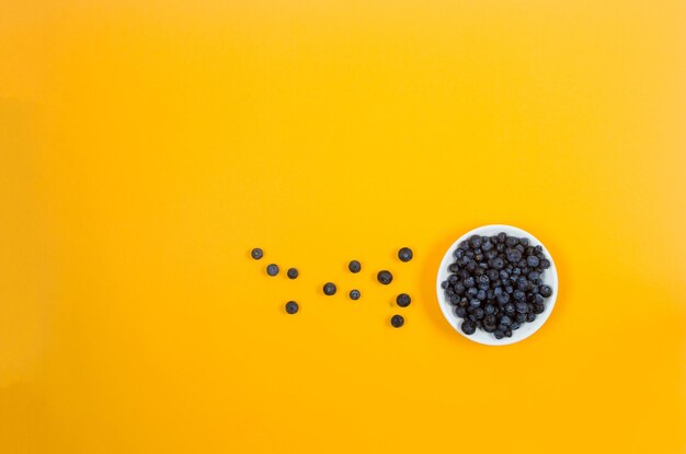 Ripe sweet blueberries on white plate on yellow background concept for healthy eating and nutrition