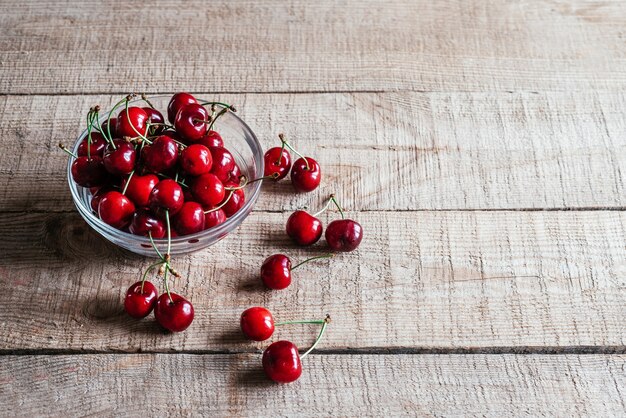 Ripe sweet cherries in a glass bowl on wooden table with green bokeh background, summer fruits