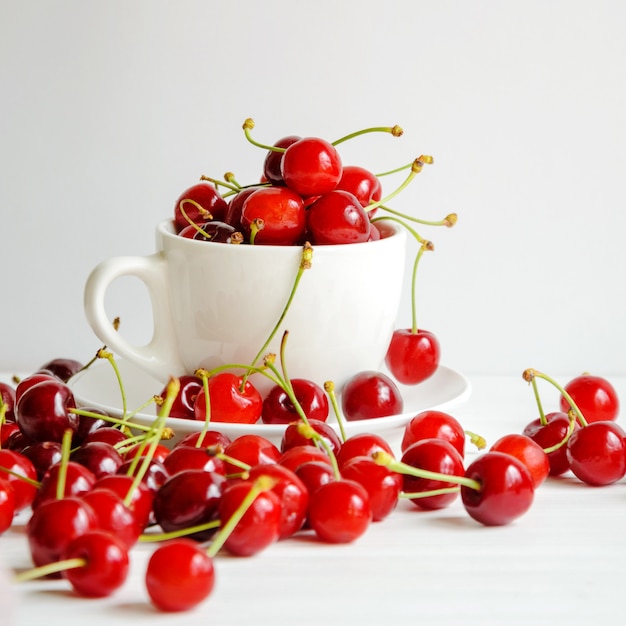 Ripe sweet cherries in a white cup on white background