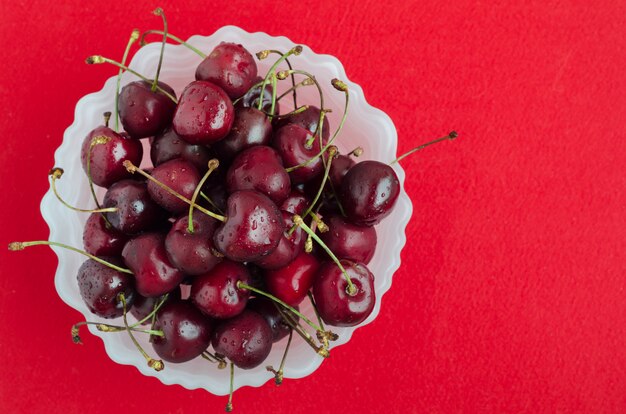 Ripe sweet cherries in white plate on red background