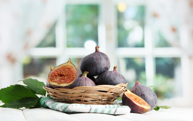 Ripe sweet figs with leaves in basket on wooden table on window background