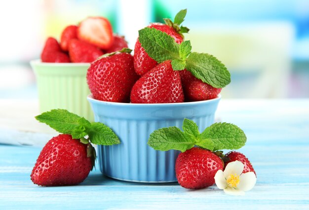 Ripe sweet strawberries in bowls on blue wooden table