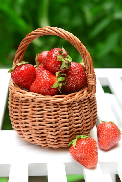 Ripe sweet strawberries in wicker basket on table in garden