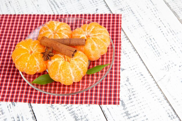 Ripe sweet tangerines with spices on color plate on napkin on wooden background