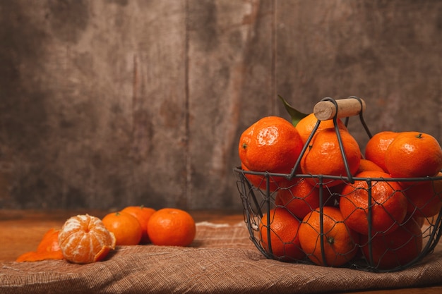 Ripe tangerines in an old metal basket on a wooden table.