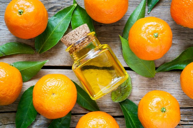 Ripe tangerines with leaves and bottle of essential citrus oil on a wooden table Top view