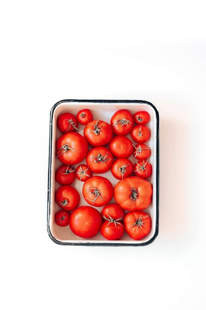 Ripe tomatoes of different sizes in an enamel bowl on the table