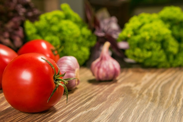 Ripe tomatoes and garlic on a wooden table with fresh herbs in the background Food Ingredients