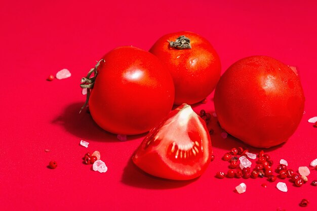 Ripe tomatoes with rose Himalayan salt and pink peppercorn. Whole and cut half vegetables, trendy hard light, dark shadow, red culinary background, copy space