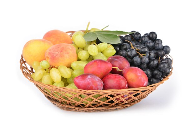 Спелые фрукты в плетеной тарелке на белом фоне