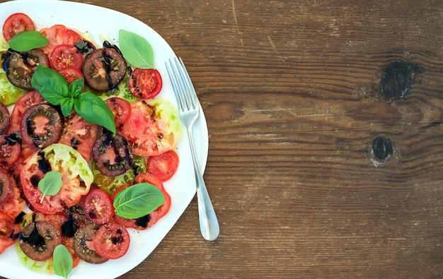 Ripe village heirloom tomato salad with olive oil and basil over rustic wooden background, top view