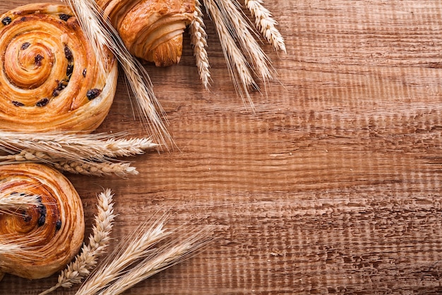 Ripe wheat ears raisin buns croissant on oaken wooden board food and drink concept