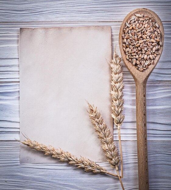 Ripe wheat rye ears corn wooden spoon clean vintage paper sheet on wood board directly above.