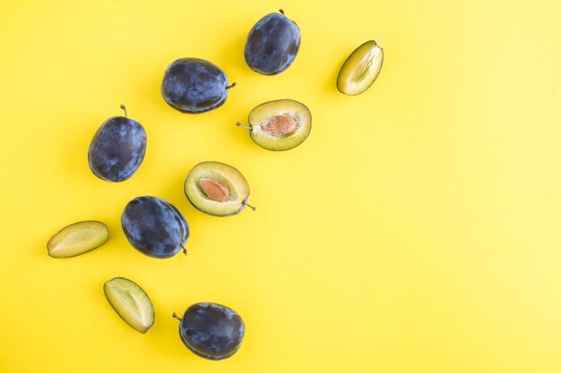 Ripe whole and cut blue plums on the yellow backgroundTop view Copy space