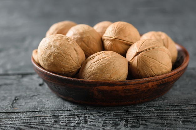 Ripe whole walnuts in a clay bowl on a dark wooden table.