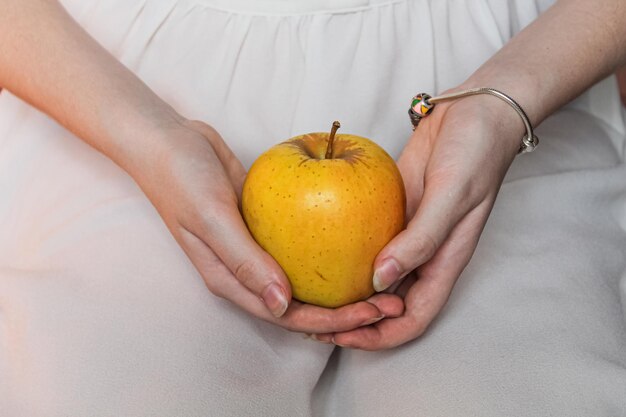 Спелое желтое яблоко в нежных женских руках