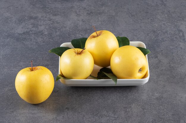 Ripe yellow apple with leaves placed on stone table . 