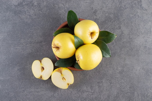 Ripe yellow apples with green leaves in clay bowl. 