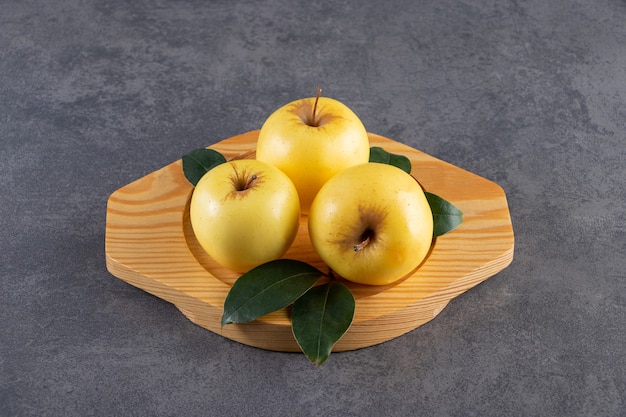 Ripe yellow apples with green leaves on wooden plate. 