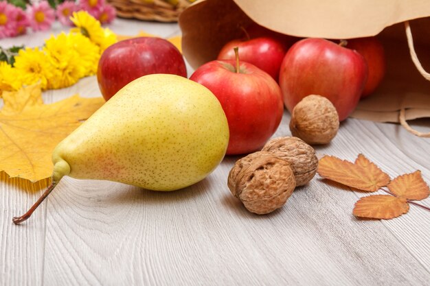 Pera gialla matura, noci, mele rosse con un sacchetto di carta, una foglia e fiori sulla scrivania in legno. cibo biologico sano. tema autunnale.