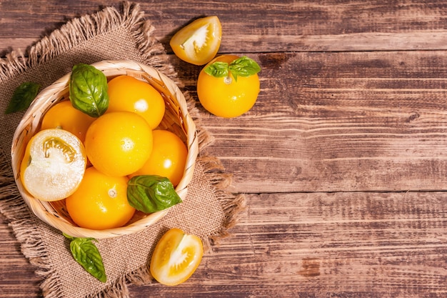 Photo ripe yellow tomatoes with fresh basil. new harvest vegetables in a wicker basket. vintage wooden table, top view