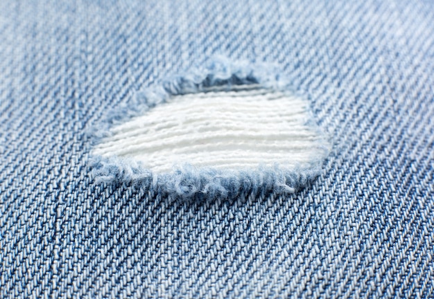 Ripped blue hipster jeans material. Destroyed denim Cloth texture. Close up.