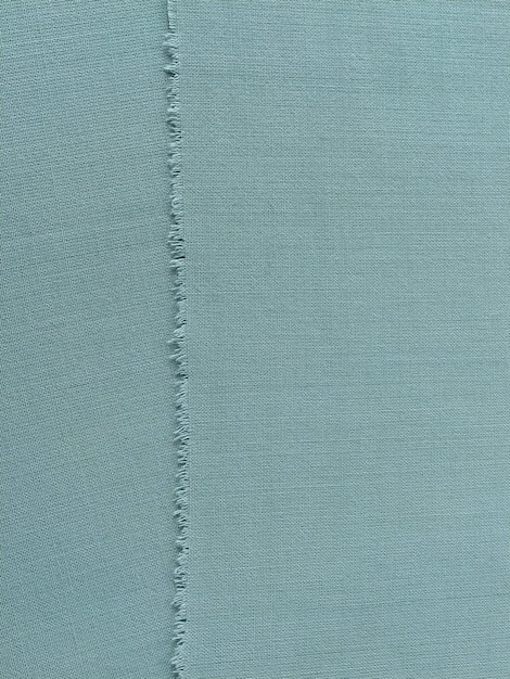 Ripped edge of fine woolen fabric in green or blue loose\
threads at the edge of a piece of textile closeup woven background\
calm green pastel color