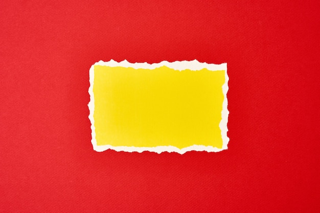 Ripped yellow paper torn edge sheet on red background. Template with piece of color paper