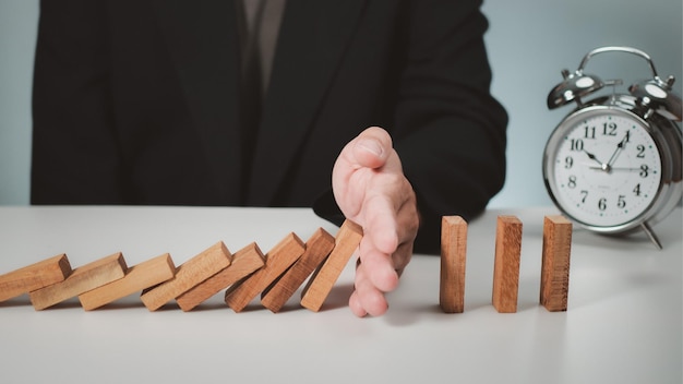 Photo risk management concept businessman hand stopping dominoes effect for business