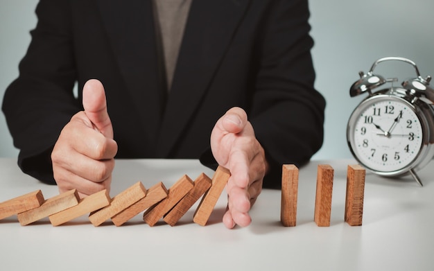 Photo risk management concept businessman hand stopping dominoes effect for business