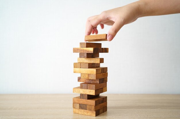 The risk will happen.Hand of engineer playing a blocks wood game on wood table vintage tone.