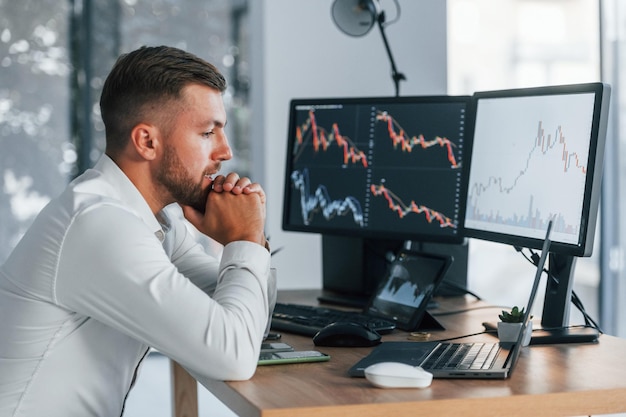 Risky job Young businessman in formal clothes is in office with multiple screens