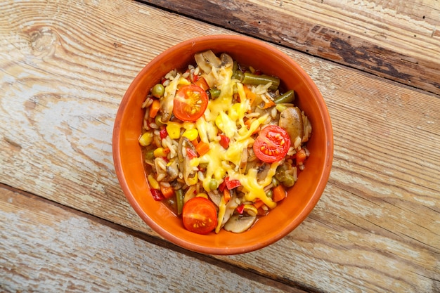 Risotto met champignons en kaas in een kleiplaat op een houten ondergrond.