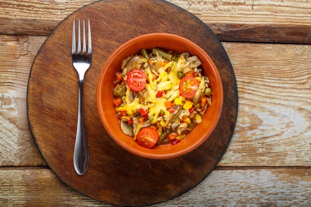 Risotto met champignons in een bord op een houten ondergrond op een houten ronde standaard naast een vork.