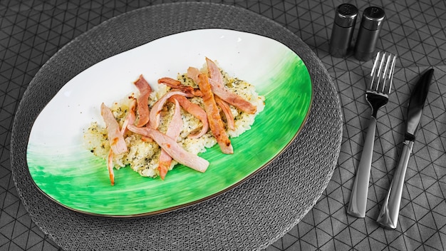 Risotto with bacon in a handmade white clay plate on a table in gray tones