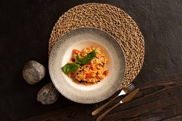 Risotto with bacon and tomatoes, garnished with basil leaves beautifully preserved by cutlery, top view.